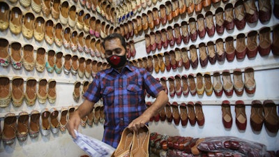 A shopkeeper dusts footwear after opening his shop after weeks, at a market area in Jammu, India