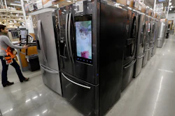 A worker pushes a cart past refrigerators.
