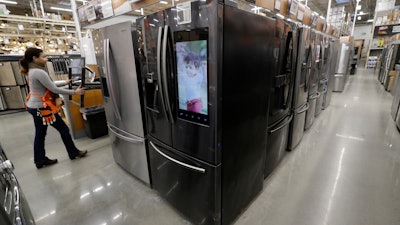 A worker pushes a cart past refrigerators.