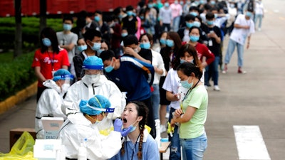 In this May 15, 2020 file photo, people line up for medical workers to take swabs for the coronavirus test at a large factory in Wuhan in central China's Hubei province. The Chinese city of Wuhan has tested nearly 10-million people for the new coronavirus in an unprecedented 19-day campaign to check an entire city.