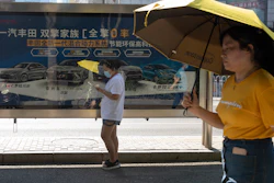 Residents pass an advertisement for Toyota hybrid cars, Beijing, Aug. 4, 2020.