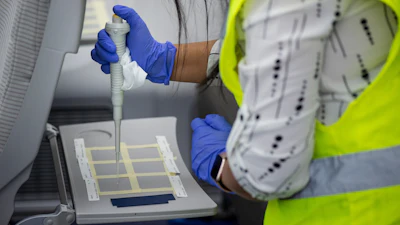 A test team member applies the safe MS2 virus on a mockup cabin tray table in first-of-its-kind test.