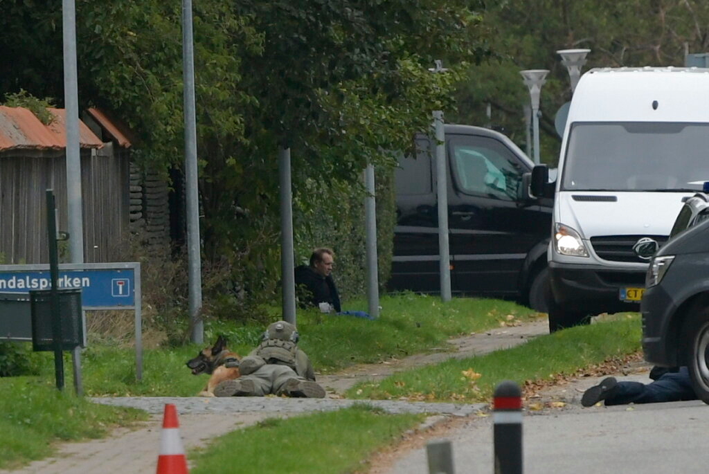 A police office watches Peter Madsen as he sits on the side of a road after being apprehended following a failed escape attempt.