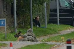 A police office watches Peter Madsen as he sits on the side of a road after being apprehended following a failed escape attempt.