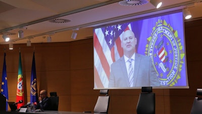 FBI Pittsburgh Special Agent Michael Christman speaks in a video presented by Portuguese police chief inspector Paulo Goncalves, at left, during a news conference at the police headquarters in Lisbon, Thursday, Oct. 15, 2020. European and American officials say that they have arrested 20 individuals for allegedly belonging to an international ring that laundered millions of euros stolen by cybercriminals in an international police operation led by Portuguese investigators and the F.B.I.
