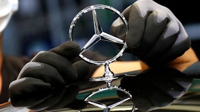 In this Thursday, April 30, 2020 file photo, an employee attaches a Mercedes emblem as he works on a Mercedes-Benz S-class car at the Mercedes plant in Sindelfingen, Germany. Daimler, maker of Mercedes-Benz vehicles, is reporting third-quarter earnings on Friday Oct. 22, 2020.