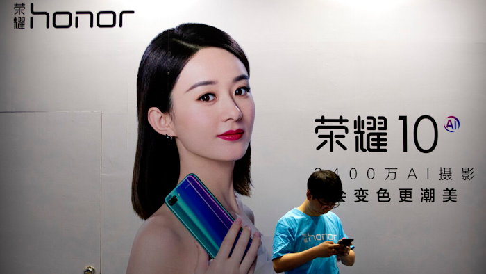 A staff member uses his smartphone in front of a billboard for Chinese smartphone brand Honor at the Global Mobile Internet Conference in Beijing, April 26, 2018.