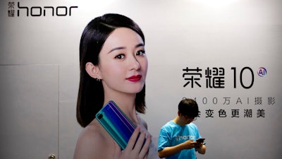 A staff member uses his smartphone in front of a billboard for Chinese smartphone brand Honor at the Global Mobile Internet Conference in Beijing, April 26, 2018.