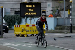 A woman cycles on a Brompton folding bicycle past a sign outside Waterloo Station reminding people they are required to wear face coverings inside the station and whilst traveling on trains, in London, during England's second coronavirus lockdown, Friday, Nov. 20, 2020.