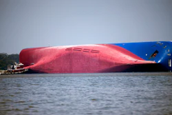 In this Sept. 9, 2019, file photo, a Moran tugboat nears the stern of the capsizing vessel Golden Ray near St. Simons Sound off the coast of Georgia. The salvage team is seeking a federal permit to surround the shipwreck with a giant mesh barrier to contain any debris when they cut the ship apart. Salvage workers coming to the Georgia coast to cut apart and remove the cargo ship that overturned will be isolated at a nearby resort to protect them from the coronavirus, officials said Tuesday, Sept. 8, 2020.