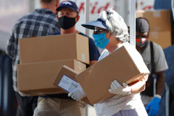 Volunteers Juanita MacKenzie, front, and Dave Stutman carry boxes of food to a waiting car at a pantry.