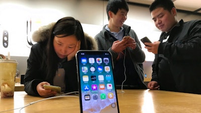 In this Monday, Nov. 6, 2017, file photo, shoppers check out smart phones at a store in Beijing, China. Companies including the Chinese arm of TripAdvisor Inc. have been ordered by regulators to overhaul their mobile phone apps in what the Chinese government says is a crackdown on pornography and other improper content.