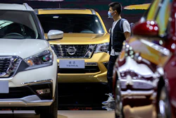 In this file photo, a visitor wearing a face mask to protect against the coronavirus walks among vehicles from Nissan at the Beijing International Automotive Exhibition, also known as Auto China, in Beijing.