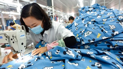 In this Oct. 27, 2020, file photo, a woman wearing a mask works in a garment factory in Donghai county in east China's Jiangsu province. China’s manufacturing activity improved in December, 2020 but at its weakest rate in three months as the economy recovered from the coronavirus pandemic while its trading partners struggled with rising infections, according to two surveys.