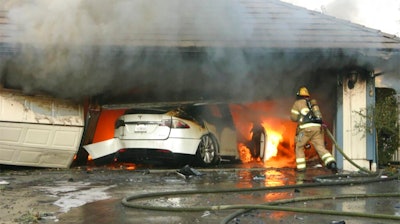 This undated photo provided by National Transportation Safety Board, The Orange County Fire Authority battles a fire on a burning vehicle inside a garage in Orange County, Calif. When firefighters removed the SUV from the garage to assess the fire , they identified the fuel source as the SUV’s high-voltage battery pack. U.S. safety investigators say electric vehicle fires pose risks to first responders, and manufacturers have inadequate guidelines to keep them safe.