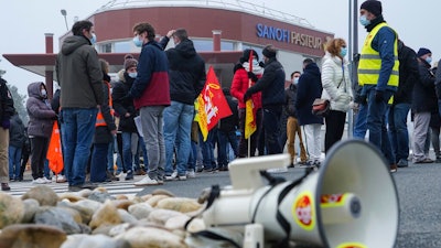 Striking workers gather outside the French pharmaceutical company Sanofi headquarters in Marcy l'Etoile, central France, Tuesday, Jan.19, 2021. Employees of pharmaceutical company Sanofi stage a protest against planned redundancies that they say could slow the fight against the Coronavirus pandemic . Sanofi had been developing Covid vaccines but will not be ready to roll out until late 2021.