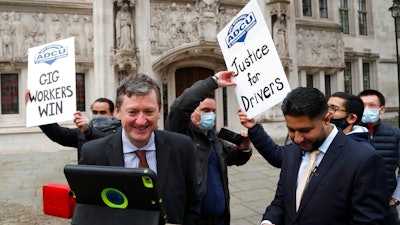 Uber drivers of the ADCU, App Drivers & Couriers Union, celebrate as they listen to the court decision on a tablet outside the Supreme Court in London, Feb. 19, 2021.