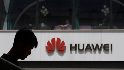 In this Thursday, May 16, 2019 file photo, a man is silhouetted near the Huawei logo in Beijing. Struggling under U.S. sanctions, Chinese tech giant Huawei has unveiled a new flagship foldable smartphone but says it will only be sold in China.