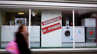 A person walks past a shop offering the repair of electronic equipment and domestic appliances in Berlin, Germany, Friday, Feb. 26, 2021. Companies that sell refrigerators, washers, hairdryers or TVs in the European Union will need to ensure those appliances can be repaired for up to 10 years. The new 'right to repair' comes into force across the 27-nation bloc Monday, March 1, 2021. The posters read: ' Repair - 24 hours'.