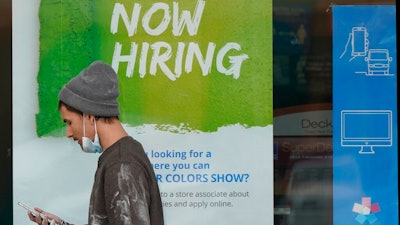 A man walks past a 'Now Hiring' sign on a window at Sherwin Williams store, Friday, Feb. 26, 2021, in Woodmere Village, Ohio. Massive fraud in the nation's unemployment system is raising alarms even as President Joe Biden and Congress prepare to pour hundreds of billions more into expanded benefits for those left jobless by the coronavirus pandemic.