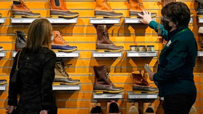 In this March 18, 2021 file photo, a salesperson helps a customer shopping for Bean Boots at the L.L. Bean flagship retail store in Freeport, Maine. Newly vaccinated and armed with $1,400 stimulus checks, Americans went on a spending spree last month, buying new clothes and going out to eat again. Retail sales surged a seasonally adjusted 9.8% after dropping about 3% the month before, the Commerce Department said Thursday, April 15.