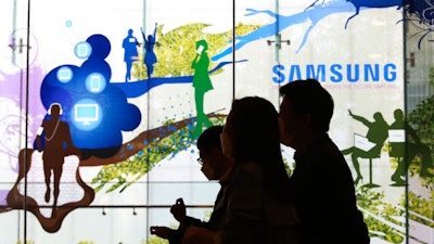 People pass by Samsung Electronics' shop in Seoul, South Korea, Wednesday, April 28, 2021. Samsung's founding family will donate tens of thousands of rare artworks, including Picassos and Dalis, and give hundreds of millions of dollars to medical research to help them pay a massive inheritance tax following last year's death of chairman Lee Kun-Hee.