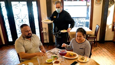 In this Wednesday, March 10, 2021 file photo, waiter Jose Bravo, center, delivers food for Alberto Castaneda, left, and his wife, Esther, at Picos restaurant in Houston. The Institute for Supply Management, an association of purchasing managers, reported Monday, April 5 that the U.S. services sector, which employs most Americans, recorded record growth in March as orders, hiring and prices all surged.
