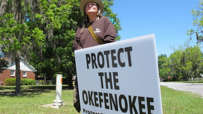 Jane Winkler stands with a sign outside a church where Georgia Gov. Brian Kemp met with local Chamber of Commerce members, Folkston, Ga., April 22, 2021.