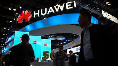 In this Oct. 31, 2019, file photo, attendees walk past a display for 5G services from Chinese technology firm Huawei at the PT Expo in Beijing. U.S. President Joe Biden has nearly doubled the list of Chinese companies whose shares are off-limits to U.S. investors in the latest sign he is not softening Washington's stance toward Beijing. Telecoms equipment maker Huawei Technologies, China’s big state-owned telecoms companies and China National Offshore Oil Corp. are on the new list of 59 companies.