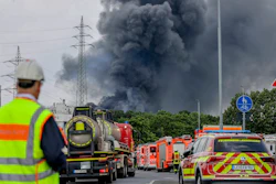 Emergency vehicles of the fire brigade, rescue services and police stand not far from an access road to the Chempark over which a dark cloud of smoke is rising in Leverkusen, Germany, Tuesday, July 27, 2021.