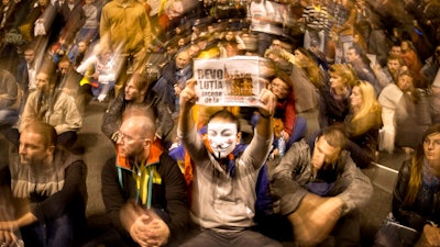 FILE - In this Sunday, Oct. 20, 2013 file photo, protesters, one wearing a mask and holding a poster that reads 'The revolution starts from Rosia Montana,' sit on the pavement, blocking the traffic, in front of the Romanian parliament during a protest against a Canadian gold mining project in Bucharest, Romania. Rosia Montana, the site of ancient Roman mining galleries in a mountainous western Romanian region and home to Europe's largest gold deposits, an estimated 314 tonnes, which was set to be exploited over a 16-year period by Gabriel Resources, a Canadian mining company that gained concession rights to the area in 1999, was added to UNESCO's World Heritage list Tuesday, July 27, 2021.