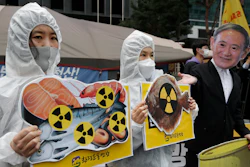 In this April 13, 2021, file photo, environmental activists wearing a mask of Japanese Prime Minister Yoshihide Suga and protective suits perform to denounce the Japanese government's decision to release treated radioactive Fukushima water, near the Japanese Embassy in Seoul, South Korea. Japan’s government adopted an interim plan Tuesday, Aug. 24, 2021 that it hopes will win support from fishermen and other concerned groups for a planned release into the sea of treated but still radioactive water from the wrecked Fukushima nuclear plant.