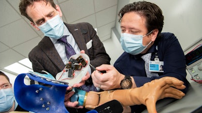 The research group in Cleveland Clinic's Laboratory for Bionic Integration looking at the inside of the touch robot system. Each small black box provides individual finger sensation to the user through a neural-machine interface.