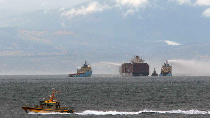 Ships work to control a fire onboard the MV Zim Kingston about 8 kilometers (5 miles) from the shore in Victoria, British Columbia, Canaeda, on Sunday, Oct. 24, 2021. The container ship caught fire on Saturday and 16 crew members were evacuated and brought to Ogden Point Pier.