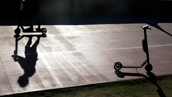 In this May 28, 2019, file photo a man on a scooter passes a parked scooter along the Mission Beach boardwalk in San Diego. San Diego is suing scooter companies to get them to pay the city's costs to defend any lawsuits generated by the two-wheeled vehicles that have proliferated on public sidewalks.