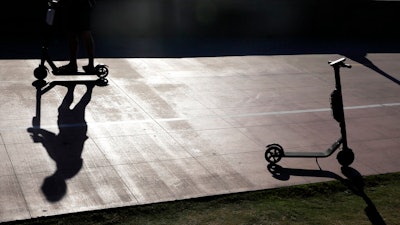 In this May 28, 2019, file photo a man on a scooter passes a parked scooter along the Mission Beach boardwalk in San Diego. San Diego is suing scooter companies to get them to pay the city's costs to defend any lawsuits generated by the two-wheeled vehicles that have proliferated on public sidewalks.