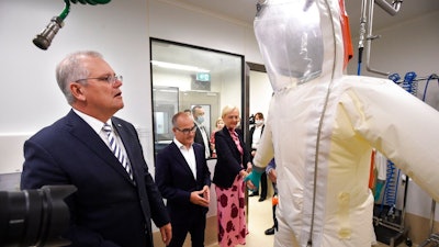 Australian Prime Minister Scott Morrison, left, looks at a hazard suit during a tour at the Peter Doherty Institute for Infection and Immunity in Melbourne, Tuesday, Dec. 14, 2021. Australia's government said Tuesday it plans to start making mRNA vaccines at home with a new plant that could produce up to 100 million doses each year.