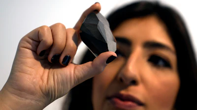 An employee of Sotheby's Dubai presents a 555.55 Carat Black Diamond 'The Enigma' to be auctioned at Sotheby's Dubai gallery, in Dubai, United Arab Emirates, Monday, Jan. 17, 2022.