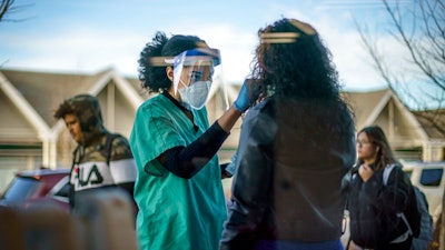 Maya Goode, a COVID-19 technician, performs a test on Jessica Sanchez outside Asthenis Pharmacy in Providence, R.I., Dec. 7, 2021. Scientists are seeing signals that COVID-19′s alarming omicron wave may have peaked in Britain and is about to do the same in the U.S., at which point cases may start dropping off dramatically.