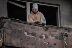 A man places a small Ukrainian flag on a burnt balcony of an apartment hit by an artillery strike, Kyiv, March 14, 2022.