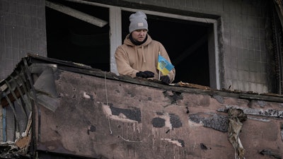 A man places a small Ukrainian flag on a burnt balcony of an apartment hit by an artillery strike, Kyiv, March 14, 2022.