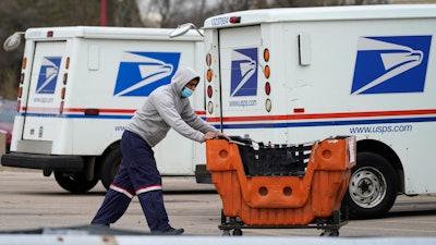 A USPS employee works outside post office in Wheeling, Ill., Dec. 3, 2021. A government watchdog said says the U.S. Postal Service's environmental evaluation used for purchases of next-generation delivery vehicles relied on some false assumptions. Jill Naamane from the Government Accountability Office told the House Oversight Committee on Tuesday that the analysis used to determine the mix of gas- and electric-vehicles overstated maintenance costs of electric vehicles and relied on gas prices that don’t reflect the current reality.