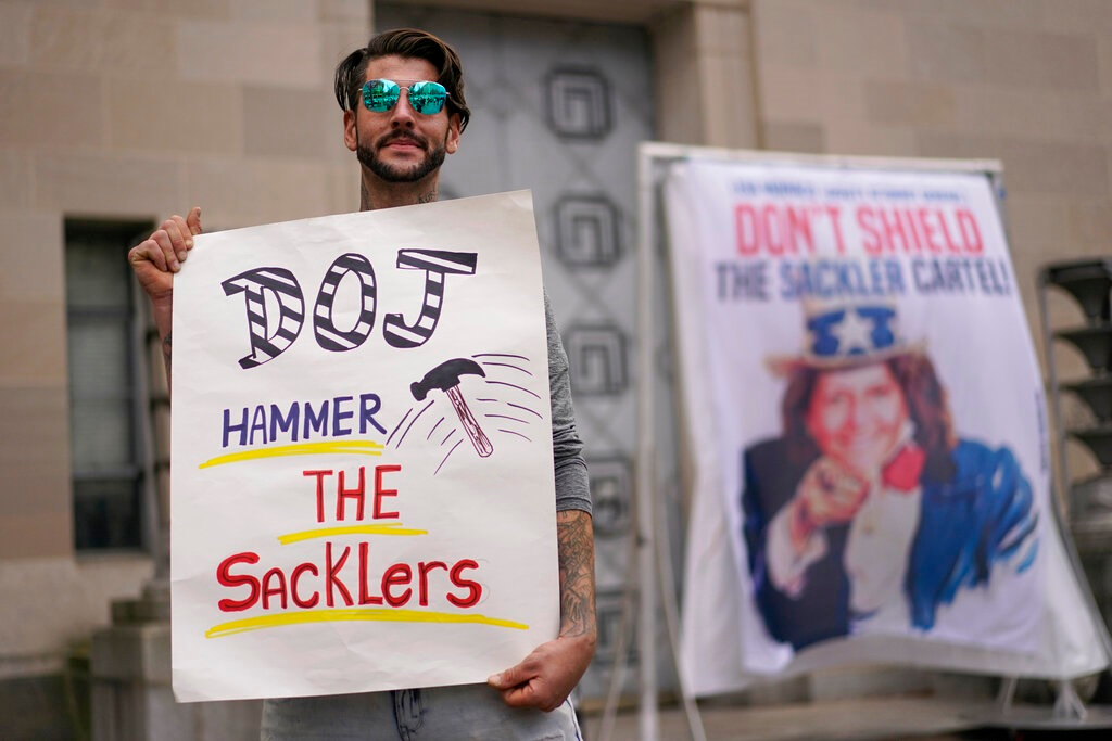 Nicholas Rivers of Maine, holds a sign that reads DOJ Hammer the Sacklers' during a protest with advocates for opioid victims outside the Department of Justice, Friday, Dec. 3, 2021, in Washington. A federal appeals panel is scheduled to hear arguments on whether members of the Sackler family can be granted protection from lawsuits as part of a bankruptcy settlement for the company they own, OxyContin maker Purdue Pharma. If the company doesn&rsquo;t get what it wants, it could have to fight off thousands of individual lawsuits.