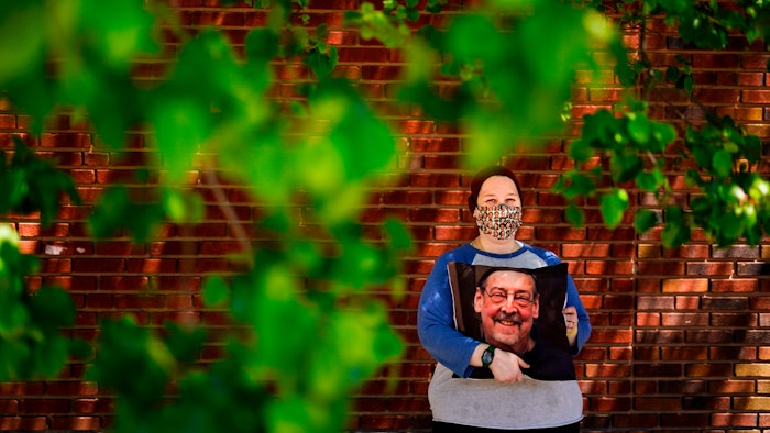 Sara Atkins poses for a photo, in Wynnewood, Pa., Tuesday, May 10, 2022, while holding a pillow with an image of her father Andy Rotman-Zaid, who died of COVID-19 in December 2020. She channels her grief into fighting for global vaccination and better access to health care to honor her father.