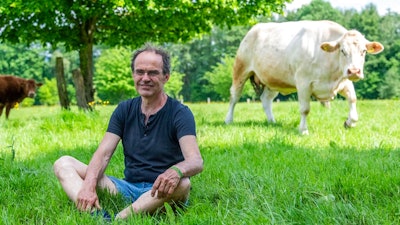 Ulf Allhoff-Cramer, farmer, sits in a pasture next to one of his cows in Detmold, Germany, Wedenesday, May 18, 2022. The organic farmer holds the VW car company partly responsible for damage to his farm. Together with Greenpeace, he wants to go to court to get VW to stop producing combustion vehicles by 2030.