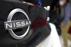 A visitor walks near a Nissan logo attached to a car at Nissan headquarters Thursday, May 12, 2022, in Yokohama near Tokyo. Japanese automaker Nissan returned to profitability in the last fiscal year for the first time in three years, despite challenges such as supply shortages caused by the pandemic and soaring costs.