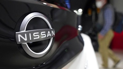 A visitor walks near a Nissan logo attached to a car at Nissan headquarters Thursday, May 12, 2022, in Yokohama near Tokyo. Japanese automaker Nissan returned to profitability in the last fiscal year for the first time in three years, despite challenges such as supply shortages caused by the pandemic and soaring costs.