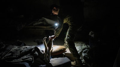 Ukrainian serviceman Anton pets a cat in a basement previously used by Russian soldiers as a temporary base in the village of Malaya Rohan, Kharkiv region, east Ukraine, Monday, May 16, 2022.