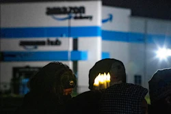 A person holds six electric candles symbolizing the six workers who died while working at the Edwardsville Amazon site in the background, during a vigil, Friday, Dec. 17, 2021, in Edwardsville, Ill., after part of the building collapsed due to a tornado the previous week before.