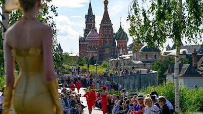 A model displays the collection by Russian designer Slava Zaitsev during the opening of the Fashion Week in at Zaryadye Park with the Spasskaya Tower and St. Basil's Cathedral in the background near Red Square in Moscow, Russia, Monday, June 20, 2022. Neither inflation nor the war in Ukraine are threatening to take a bite out of the luxury fashion market, according to a study published Tuesday, June 21, 2022.
